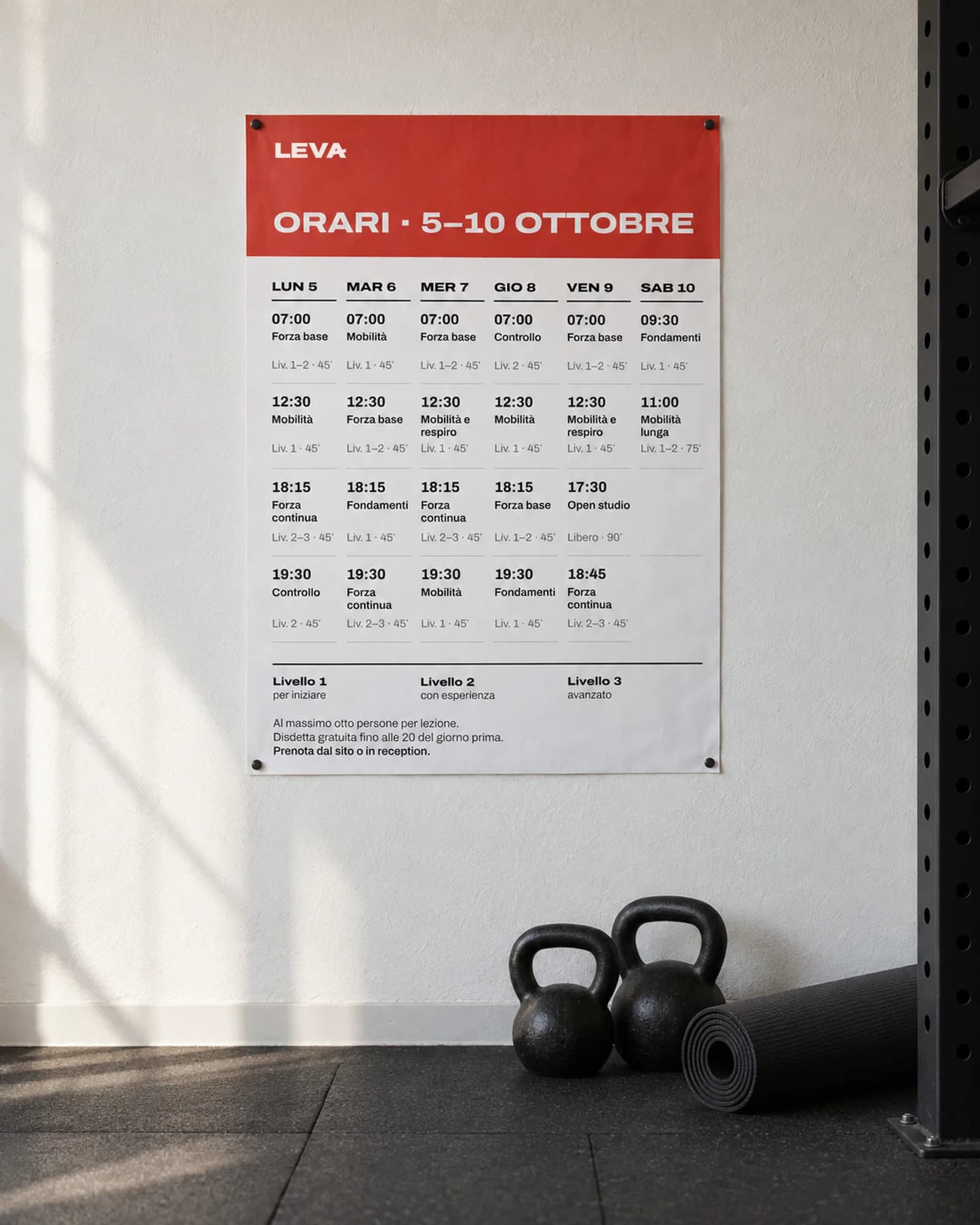 Calendario A3 Leva appeso alla parete di una sala d'allenamento, con due kettlebell a terra